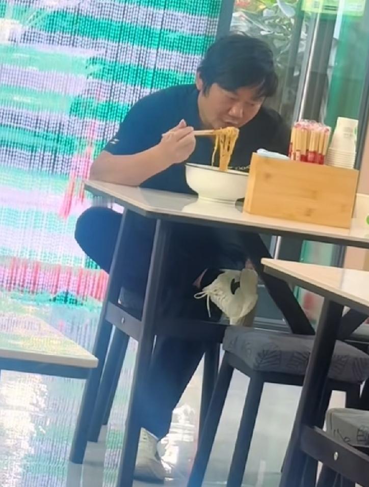 张雪在吐鲁番街头面馆吃牛肉面。非常接地气，其貌不扬，翘着二郎腿，边嗦面、边看手