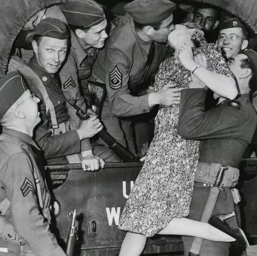 1940年代，一名士兵举起一名年轻的女人，将她送给卡车上的大兵。这名大兵不但亲吻