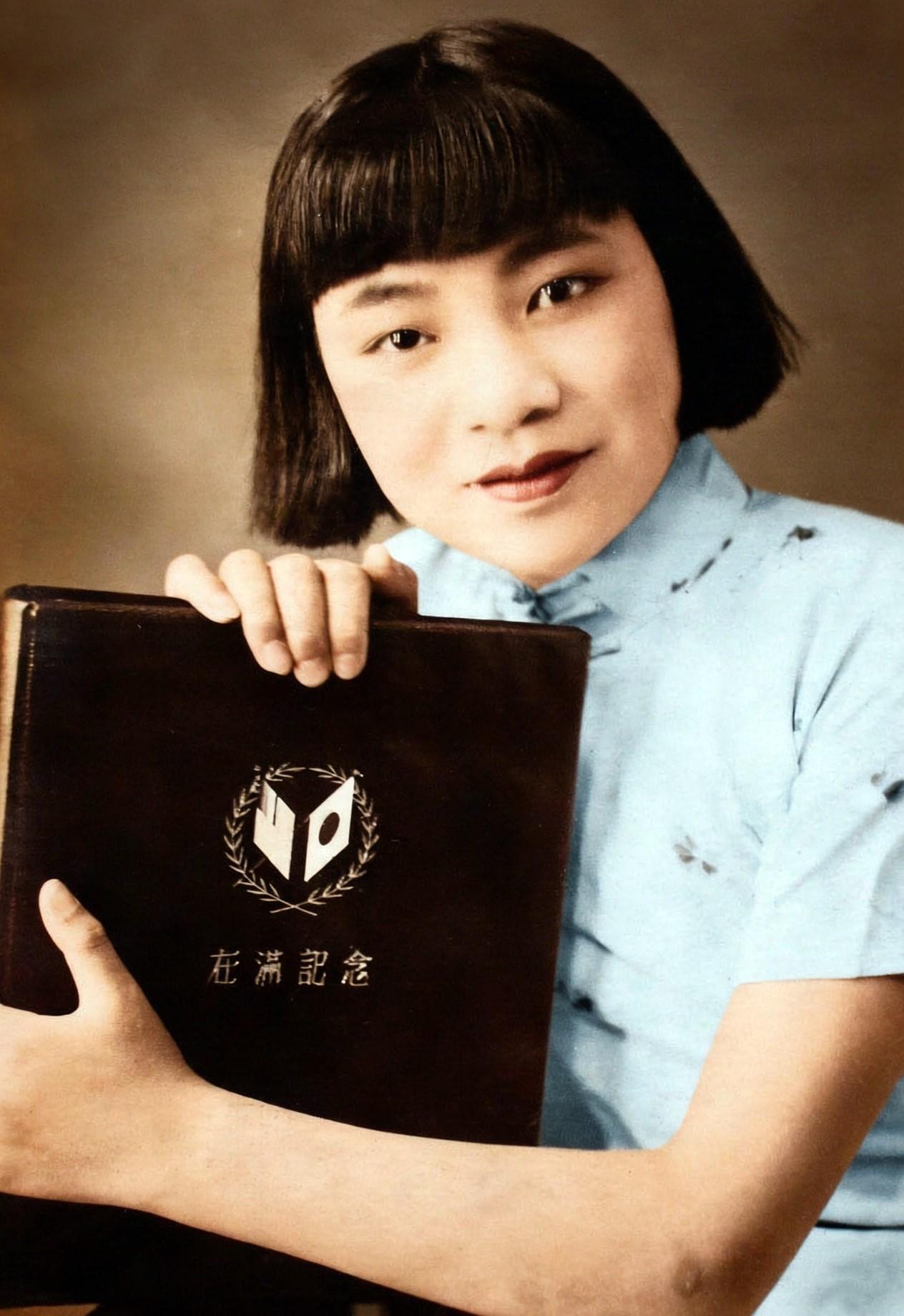 伪满洲国时期，中国东北。一名浓眉大眼的年轻女子肖像，手里捧着一本封面印有“在满纪