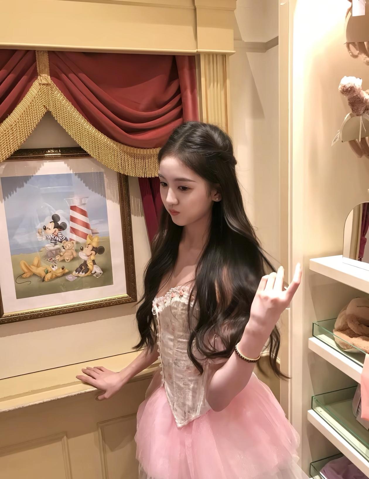 女孩穿着粉色裙子，站在米奇画前。