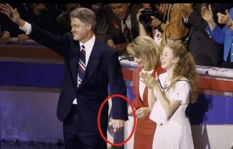 左图中的克林顿穿着深色的西装，系着蓝白条纹领带，潇洒帅气，春风得意，朝向人群挥舞