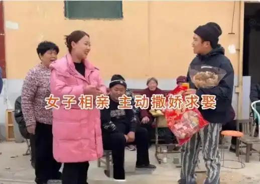 院子里围满看热闹的乡亲，小伙提着礼品刚坐下，对面穿粉色棉衣的女子主动上前拉住他。