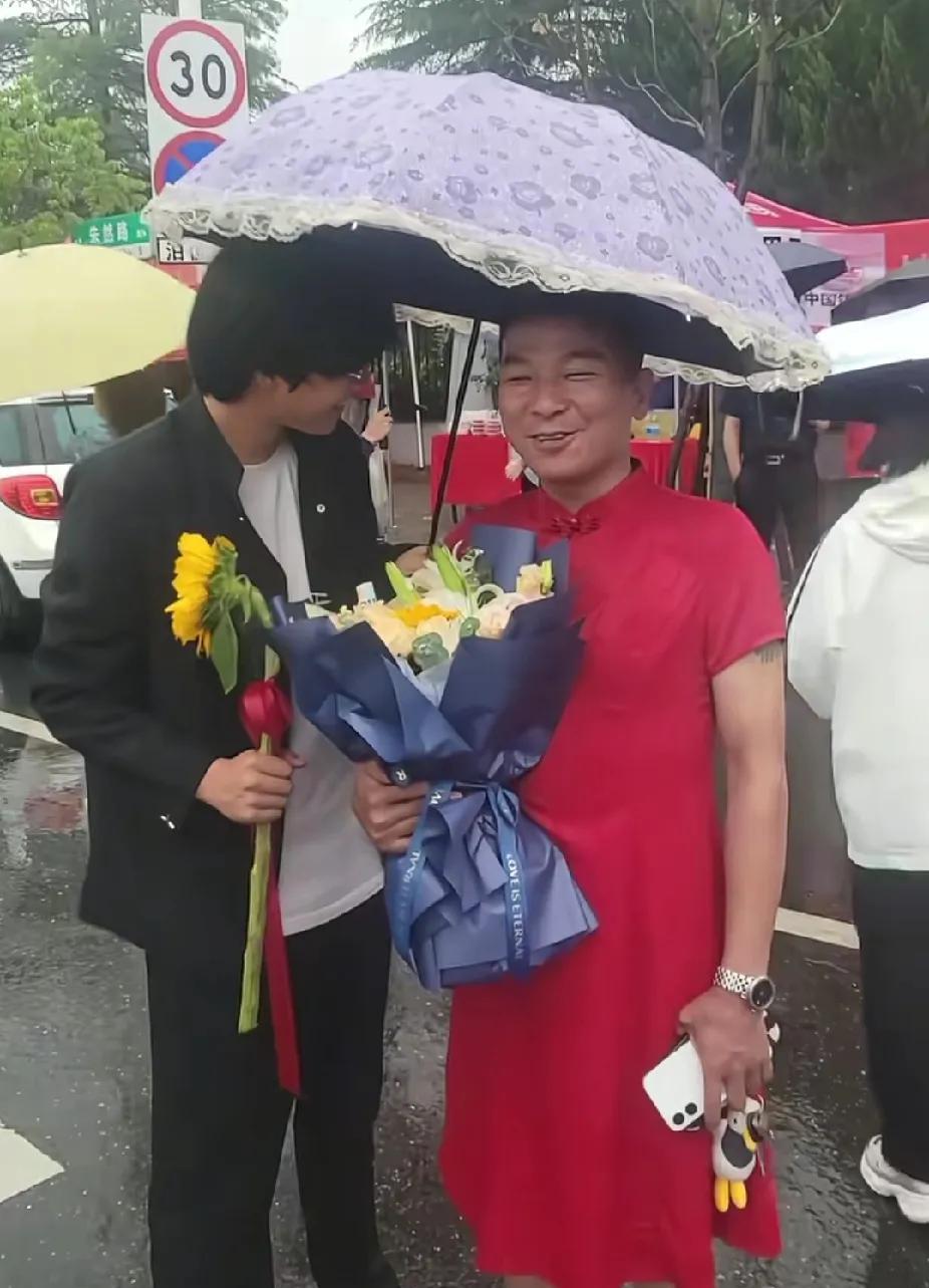 一名穿着大红旗袍，抱着鲜花和向日葵的男子，突然出现在男孩面前，男孩笑着笑着就掉泪