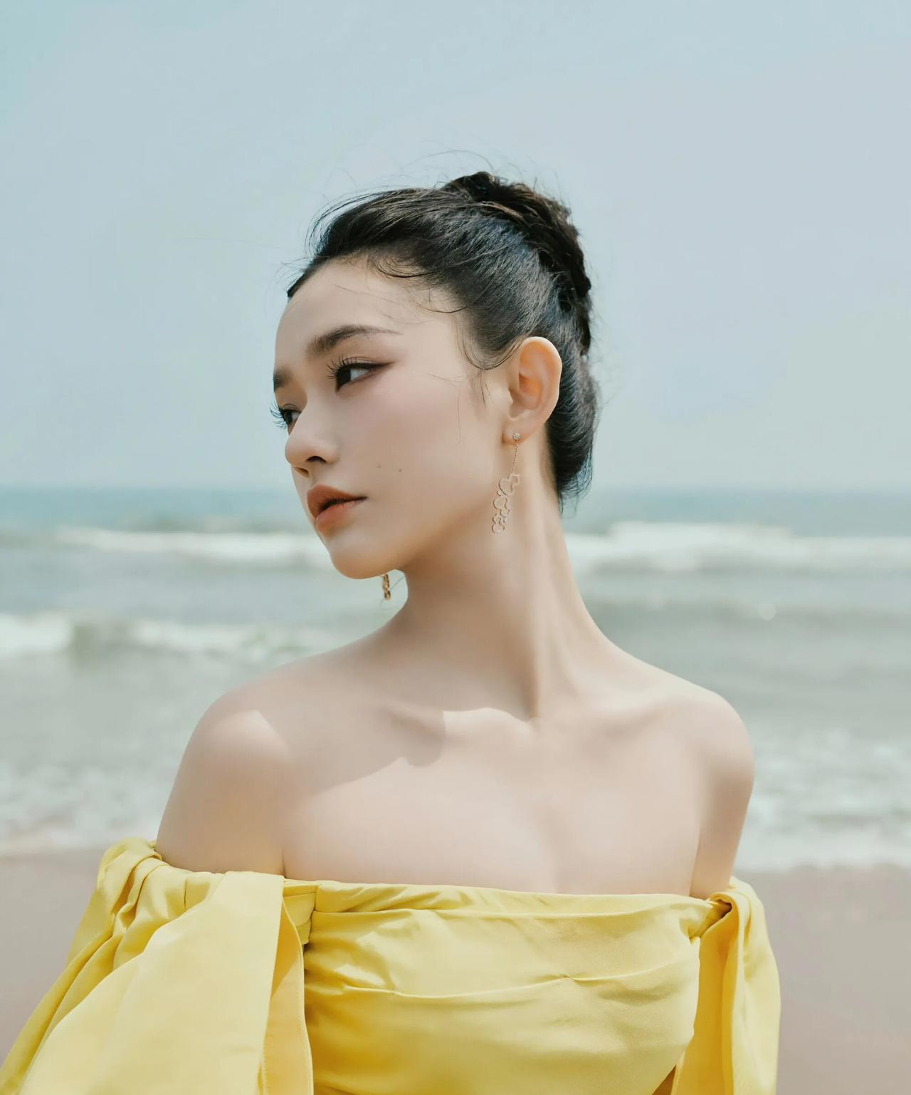 林允漫步海边，一袭明黄露肩裙轻盈灵动，蓬松袖摆随海风轻扬。海浪作伴，沙砾为席，她