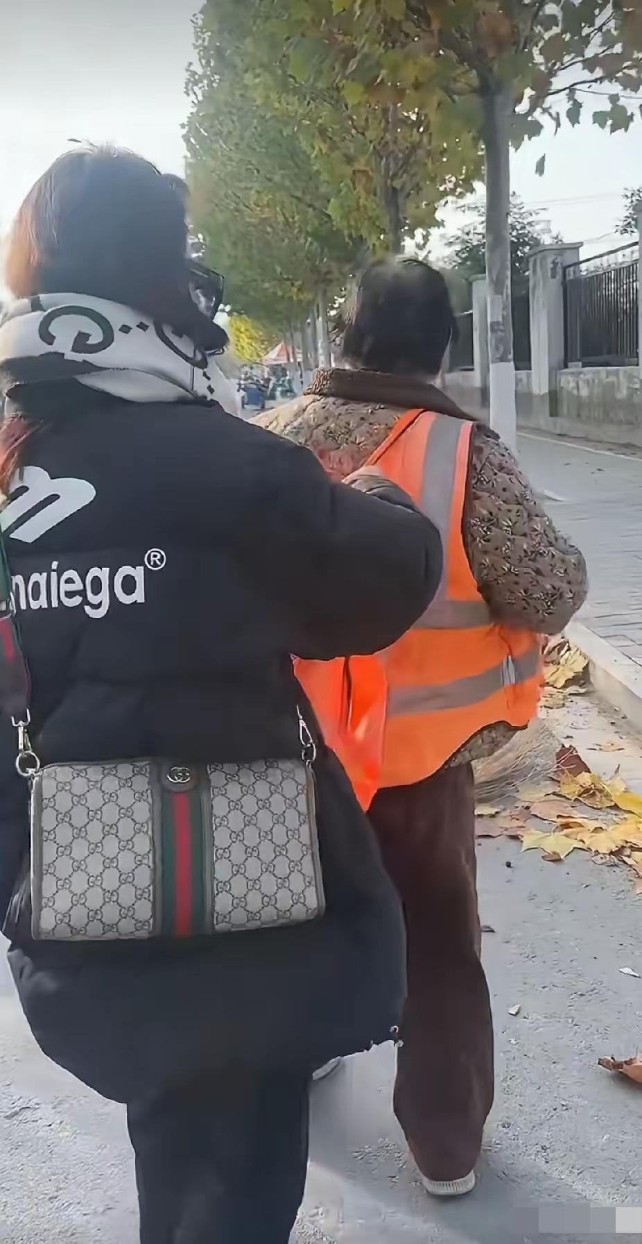 环卫工阿姨正在清扫地上的落叶，一名年轻女子突然走过去脱掉了阿姨身上的工作服，接下