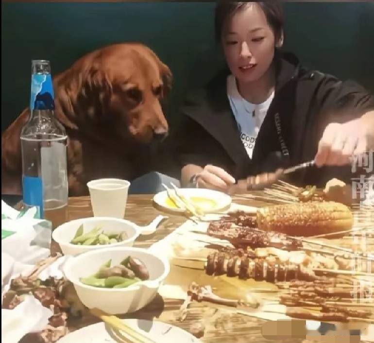 5月10日大连市金州区一个烧烤店内，一女子在餐桌上喂狗子肉串！女子坐在体型庞
