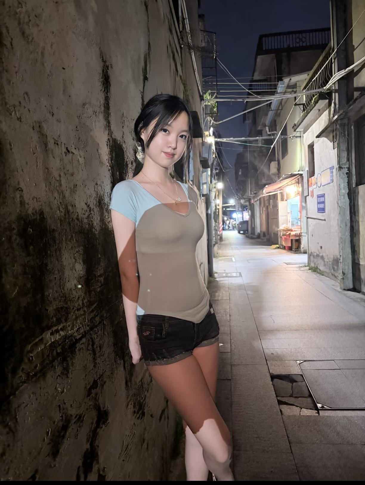 女孩在夜晚的小巷子里微笑的靠墙站着。
