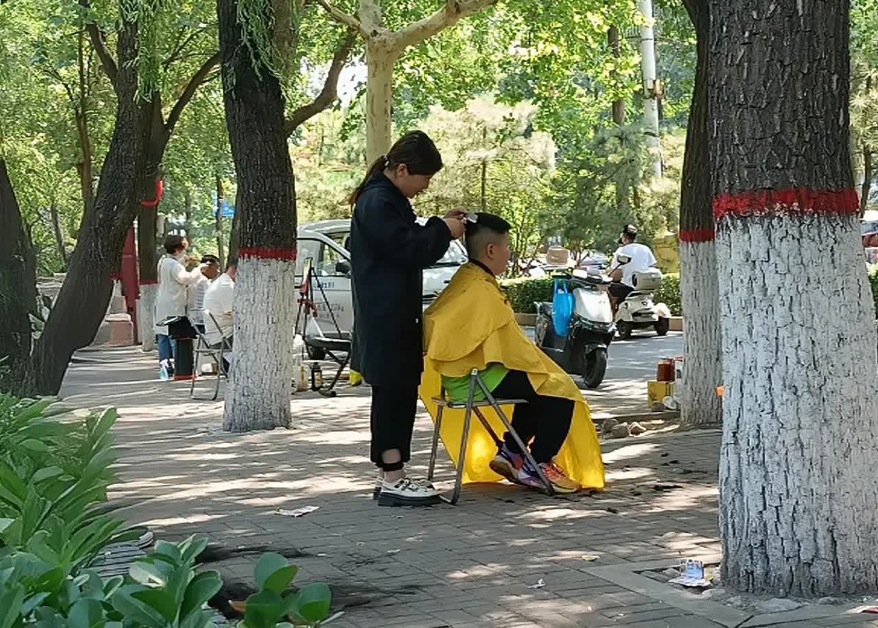 从前年开始，公园里就开始出现了低价理发的摊位。今年，摊位越来越多，整个公园按