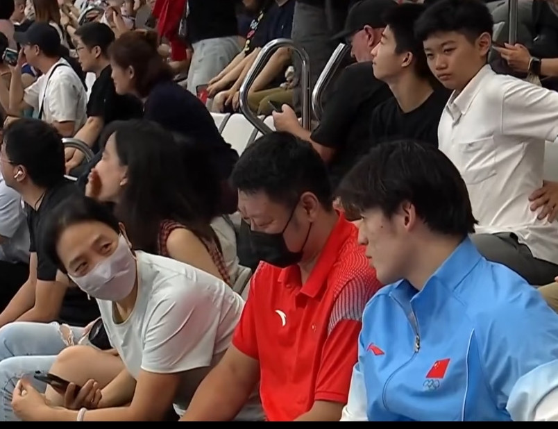 张展硕的父母也来见证儿子在亚运会的第七金了，夫妻俩很低调，戴着口罩坐在观众席，和身旁的游泳运动员一起