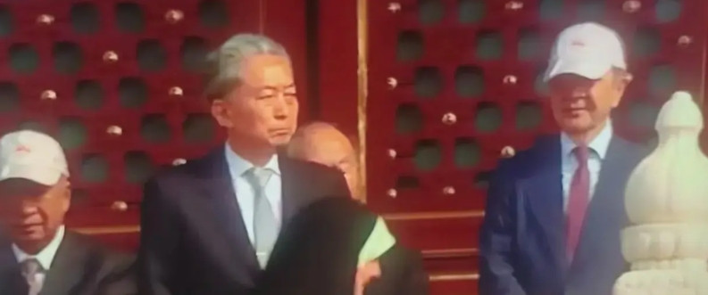 镜头给到日本前首相鸠山由纪夫，看他和身旁的人对比，感觉到他有种闷闷不乐的感觉。在
