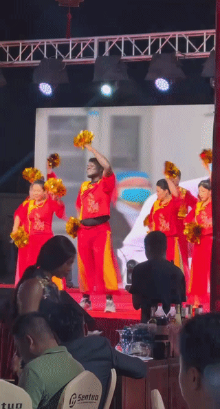 一名黑人男子站在舞台上领着大爷大妈跳舞。看起来跳的非常卖力，真是深受大家的喜爱