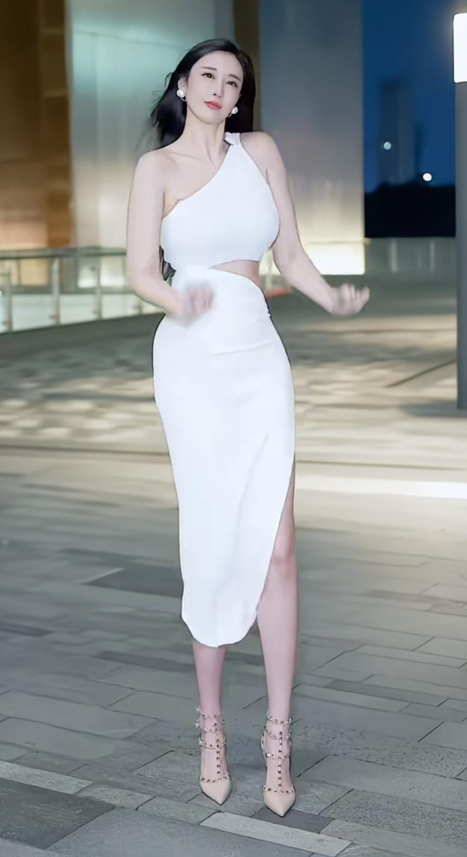 夜色为幕，白裙似光。单肩设计勾勒优雅肩线，腰侧镂空与裙摆开叉尽展灵动，铆钉高跟鞋