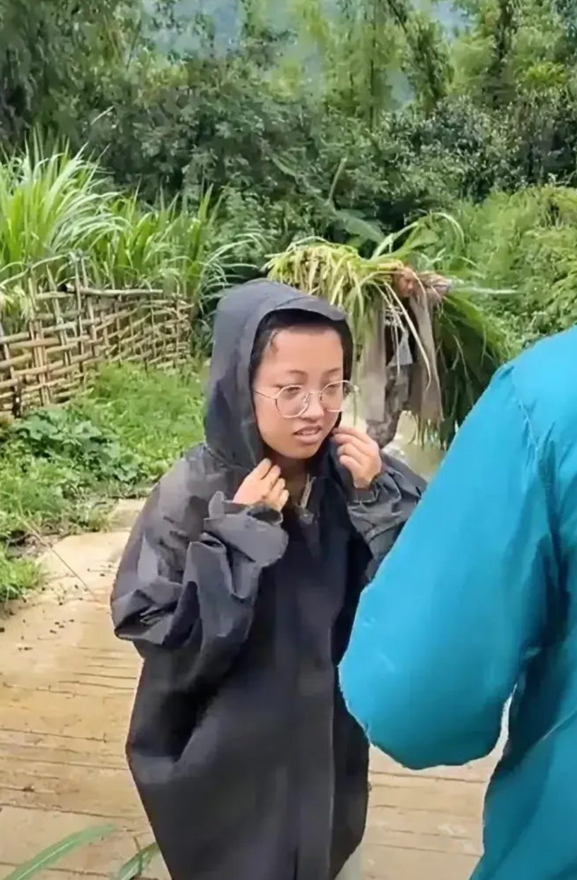 云南临沧一女孩帮家人从山里割了一捆牛草，正穿雨衣扛着回家，这时对面走过来了一个邮