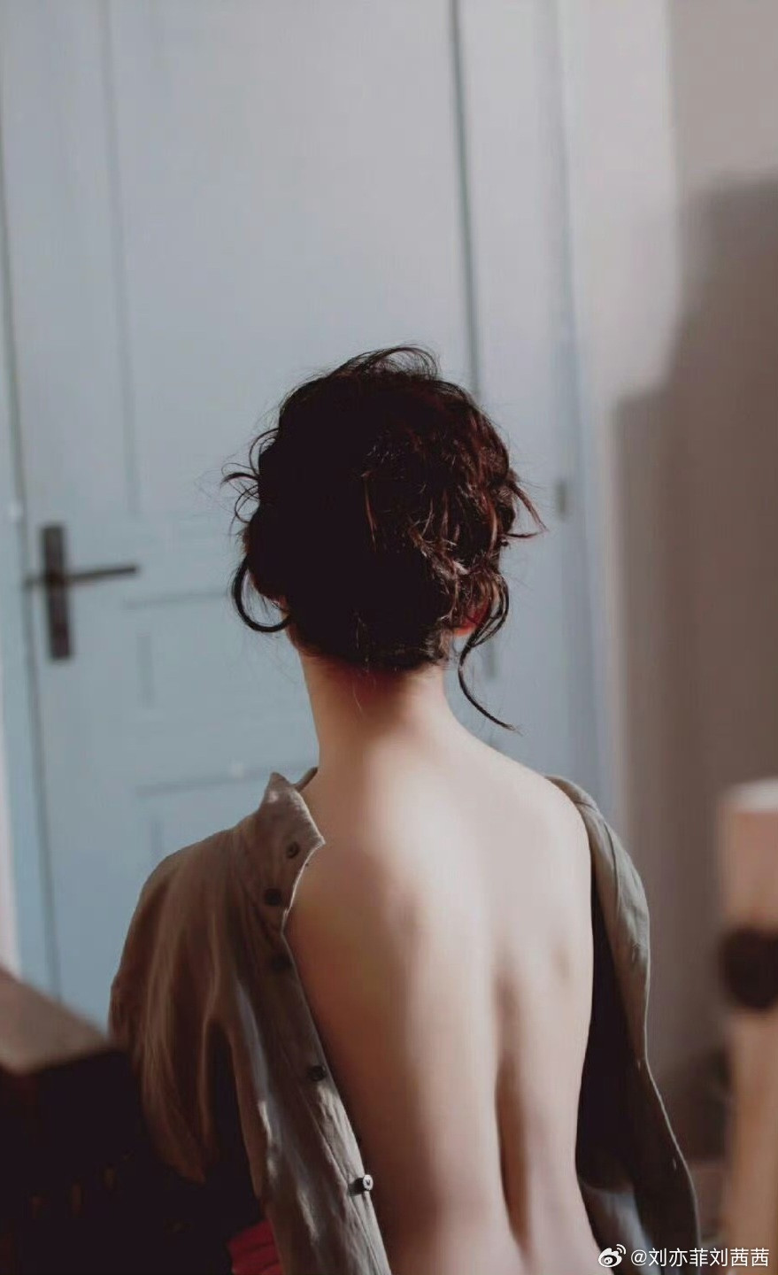 刘亦菲身着一件宽松的浅灰色棉麻衬衫，衬衫被刻意斜搭、半敞，一侧滑落肩头，露出大片