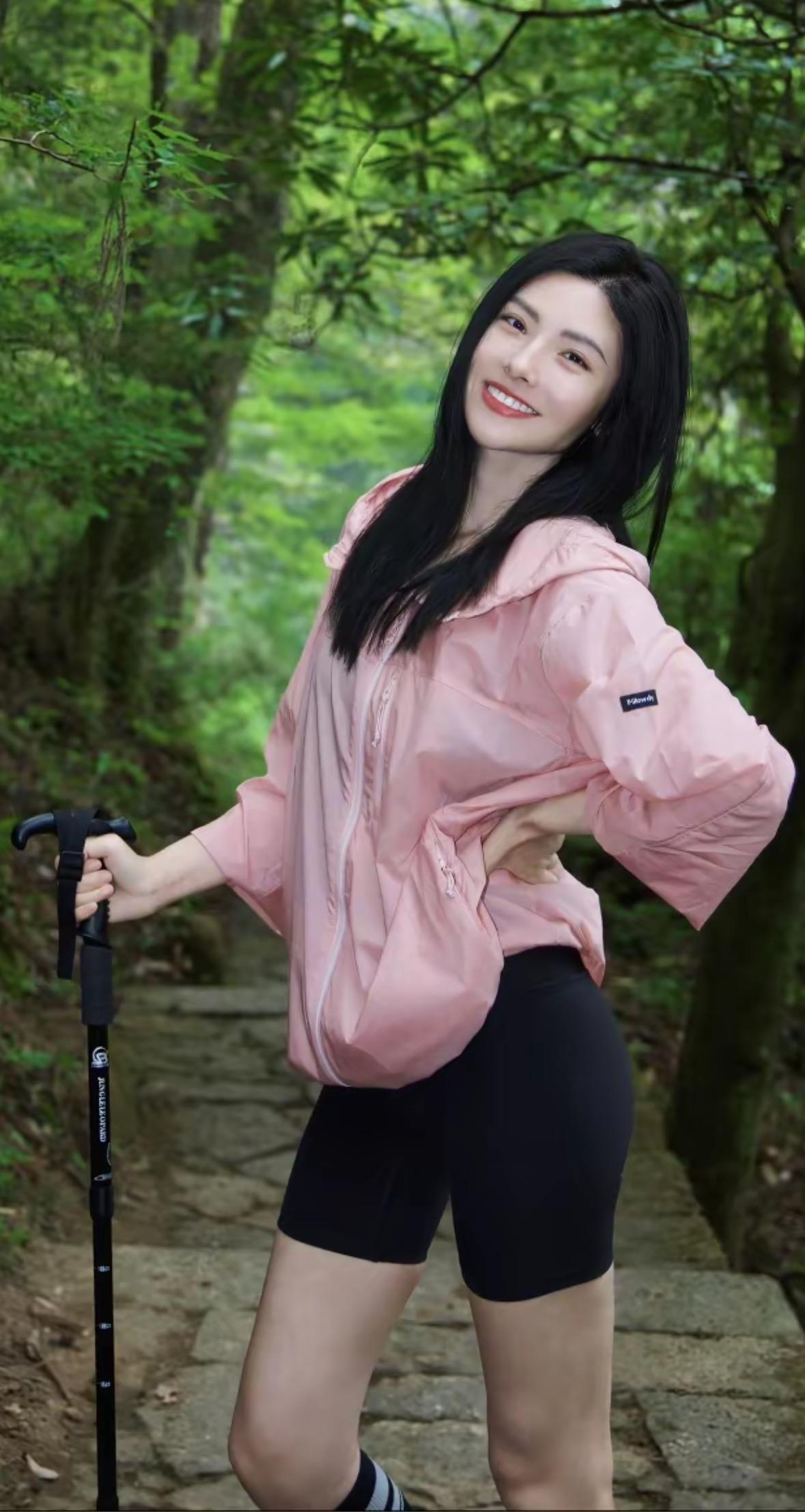 我举着登山杖站在岩壁前，粉色外套被山风吹得鼓成充气球。朋友在山下喊："拍张照发朋