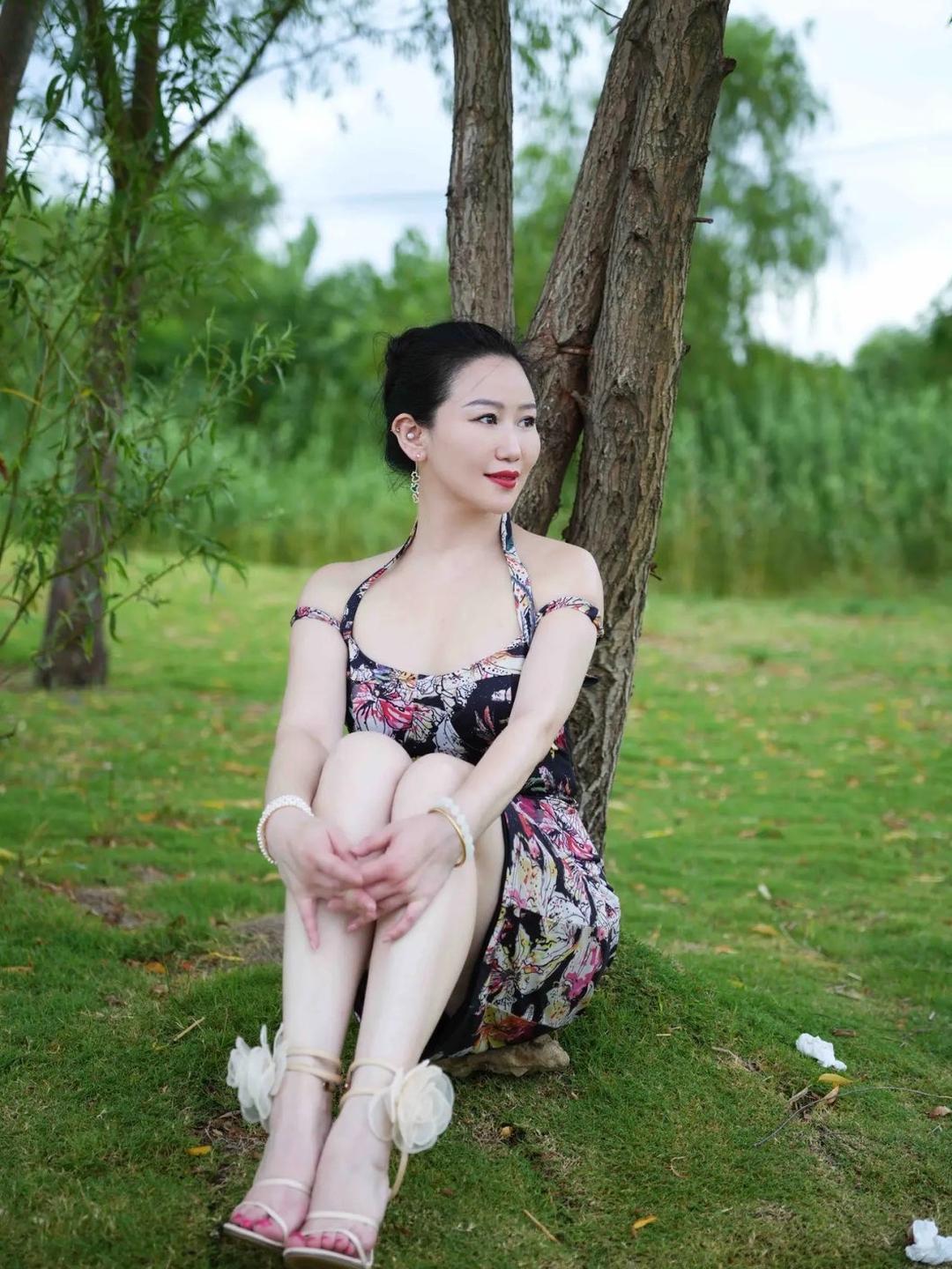 郊外草坪绿意盎然，满眼清新草木衬得氛围温柔治愈，黑底碎花挂脖短裙韵味十足，修身版