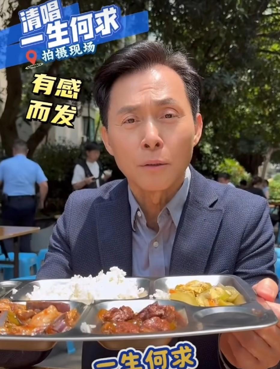 香港演员张国强在片场享用盒饭。他身着西装革履，坐在小板凳上，就着剧组分发的盒饭大