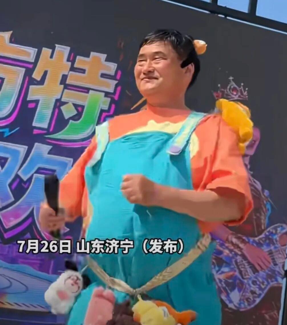 朱之文大衣哥身穿天蓝色背带裤，橘色文化衫，头上还别着一个黄色玩偶，大热天在舞台上