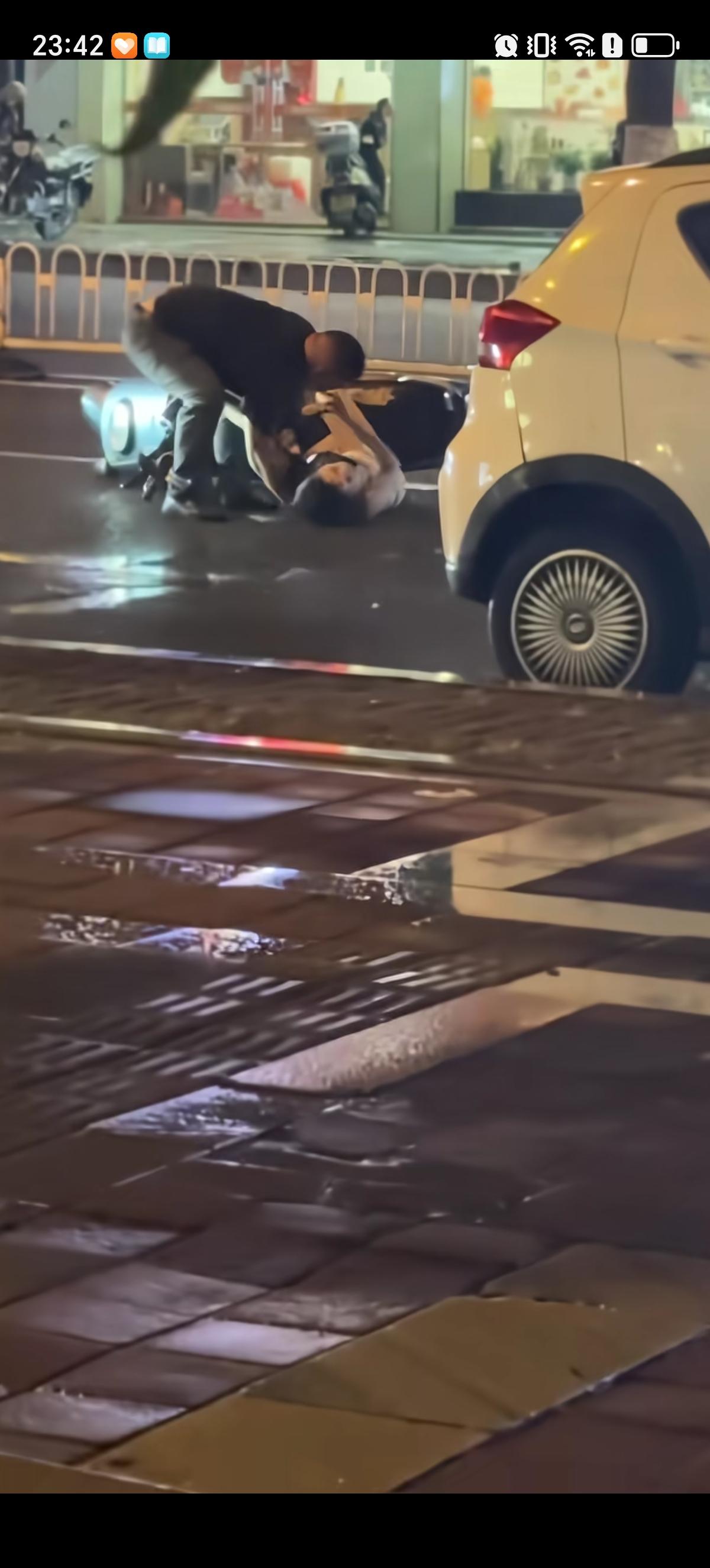 在深夜雨天湿滑的地面上躺着一位从逆行从电动车上摔下来的白色包臀裙长发女子。一大哥