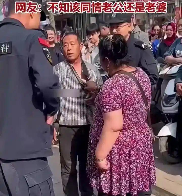 集市大街上围满看热闹的路人，安保人员赶来调解，场面乱作一团。碎花裙女子死死拽住丈