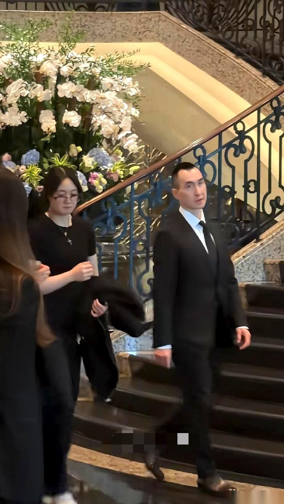 赌王儿子何猷龙，带妻女出席葬礼。一家三口，黑衣肃穆。他全程黑着脸，眉心拧成个疙