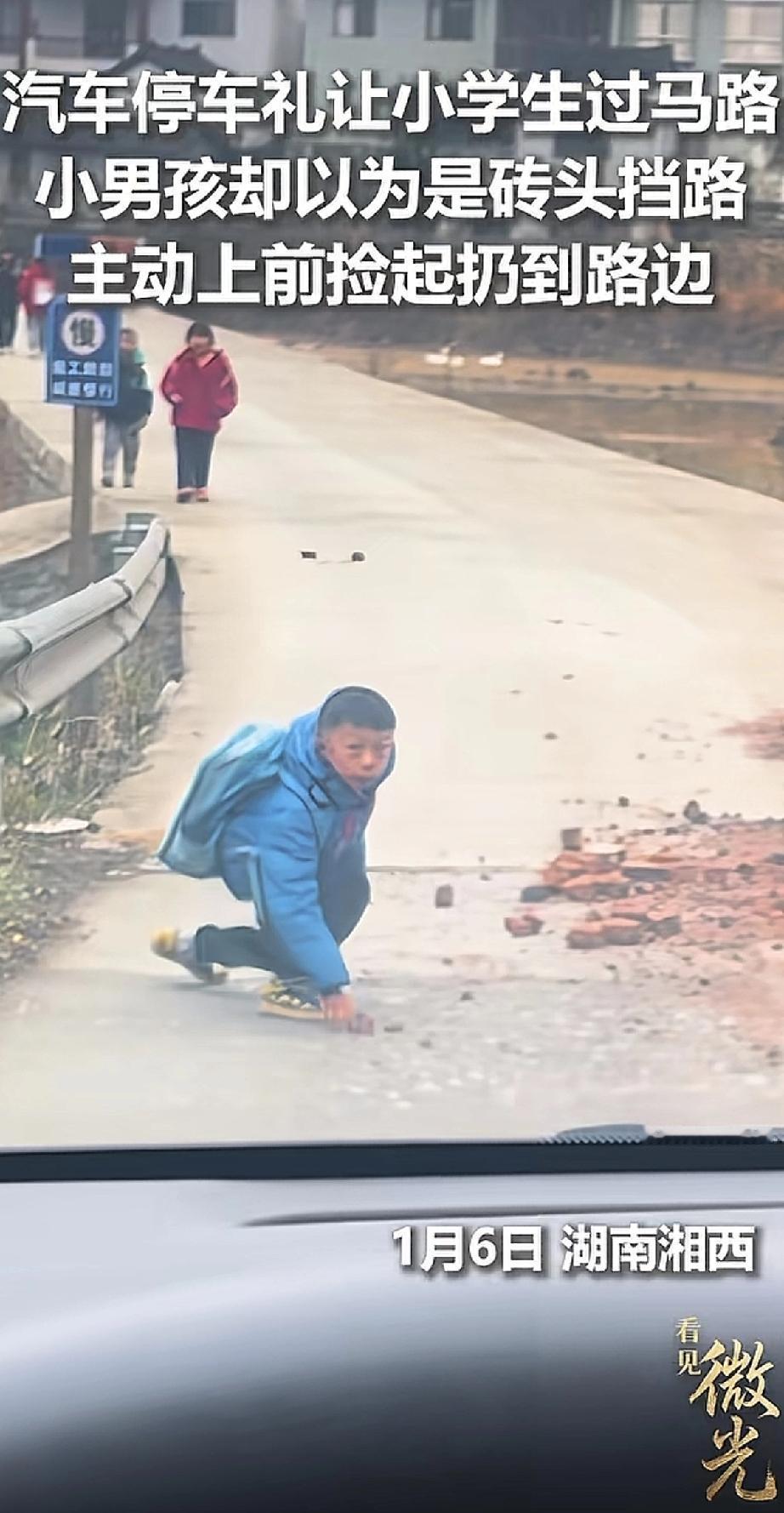 一辆车在乡村路停下，礼让一群小学生过马路。走在最后的小男孩，看到车停在自己面前，