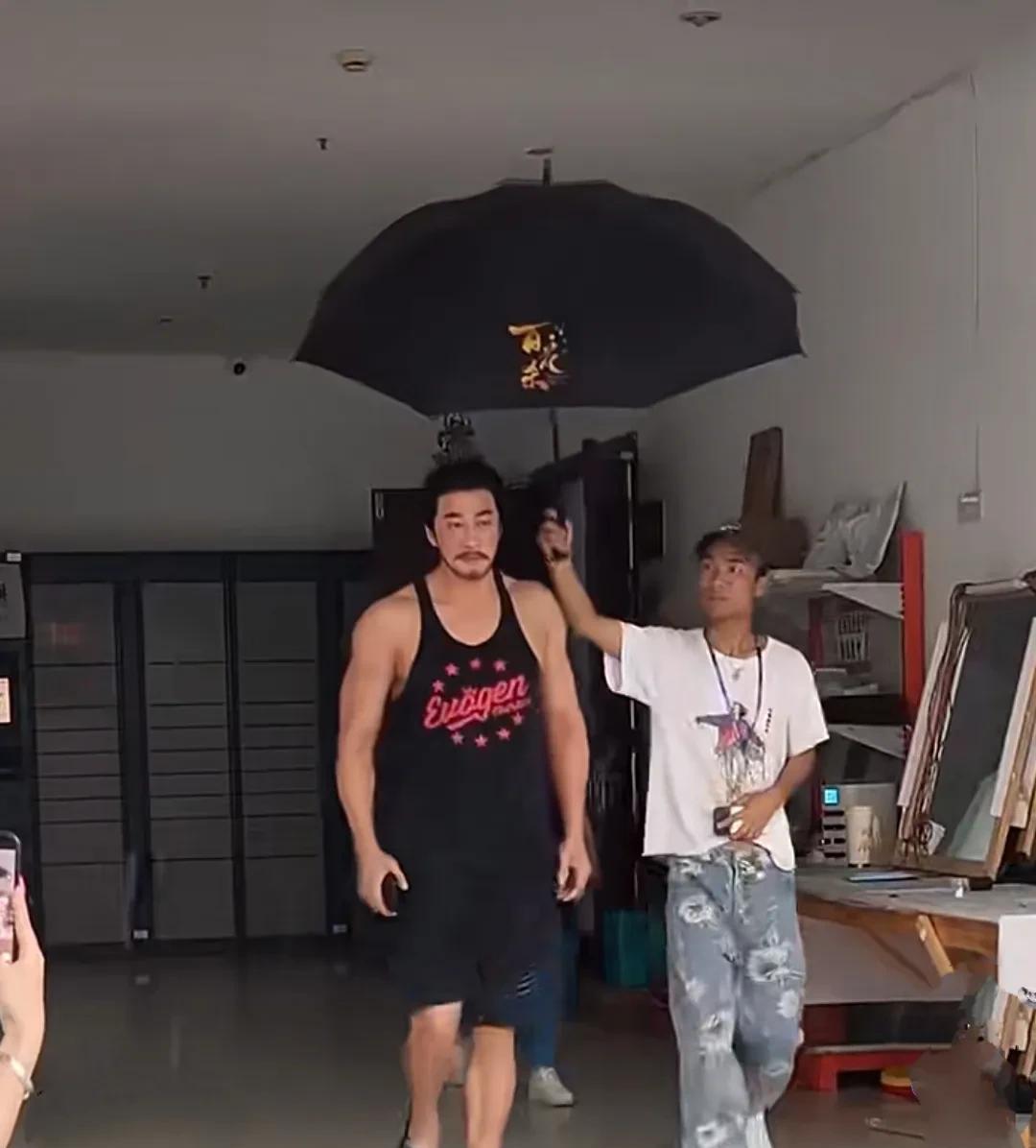 型男何润东近日现身，头束古装发型，一脸络腮胡子，上穿黑色吊带背心，黑色短裤，拖鞋