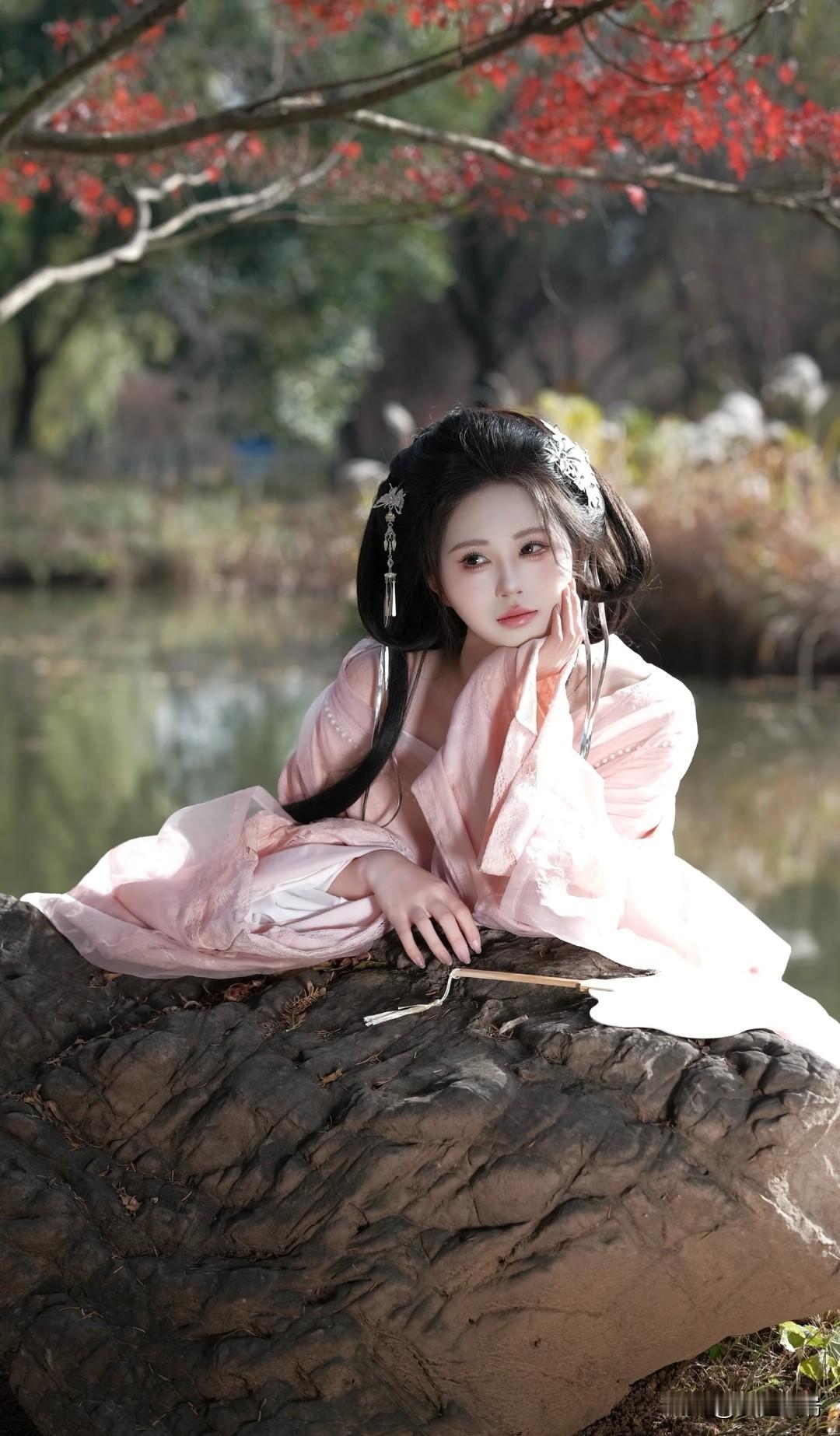 粉衣少女倚石畔，红叶映水如画卷。