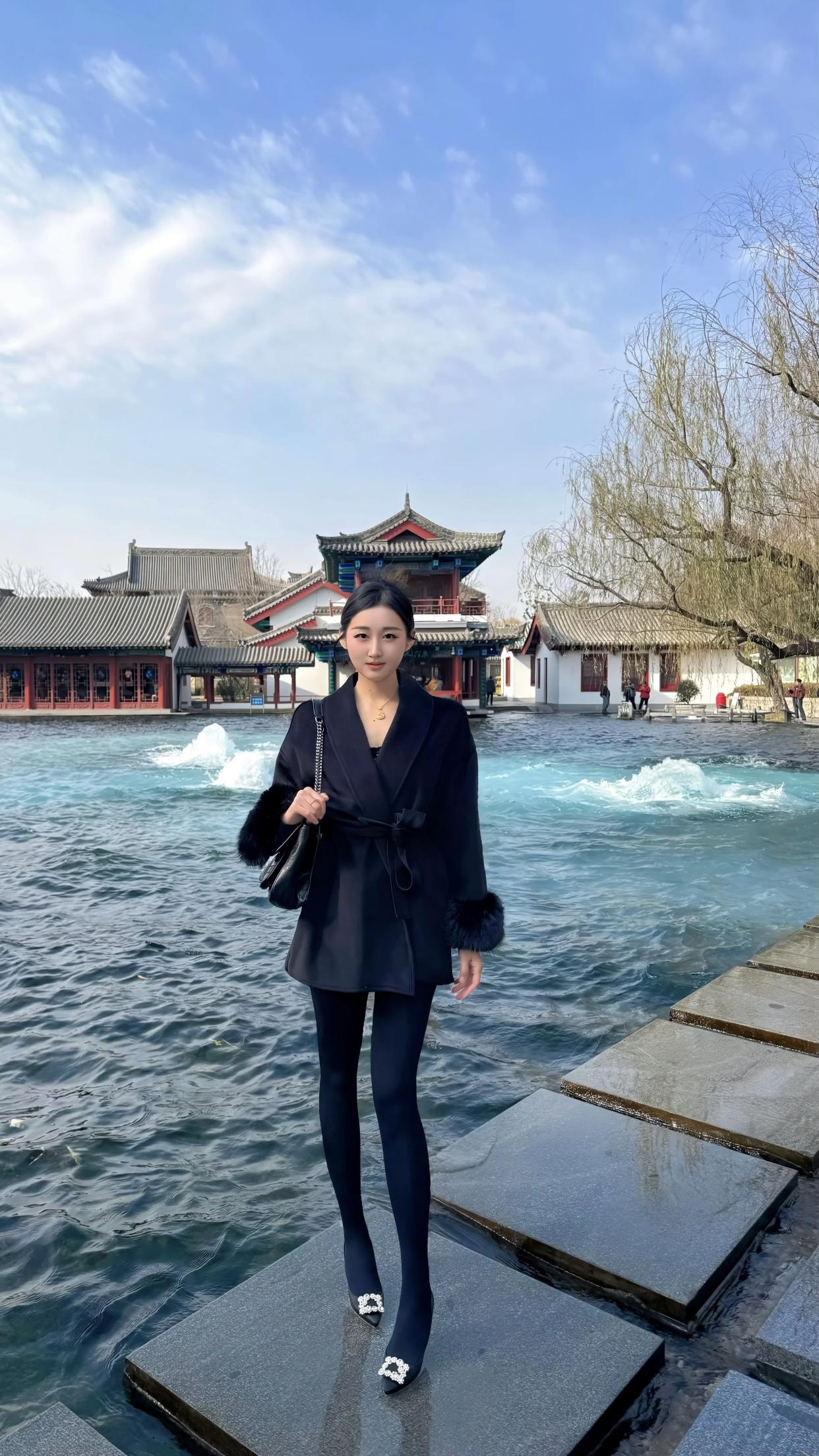 女人怎样穿搭，更显气质冬日暖阳下的优雅穿搭，黑大衣与蓝水景的完美融合。