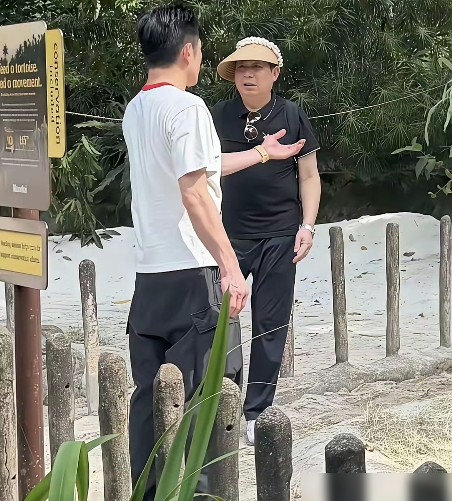 61岁郭富城和59岁岳父同框，岳父给他背包打伞，网友炸了。这画面搁谁都得多看两眼。郭富城黑衣黑裤，身