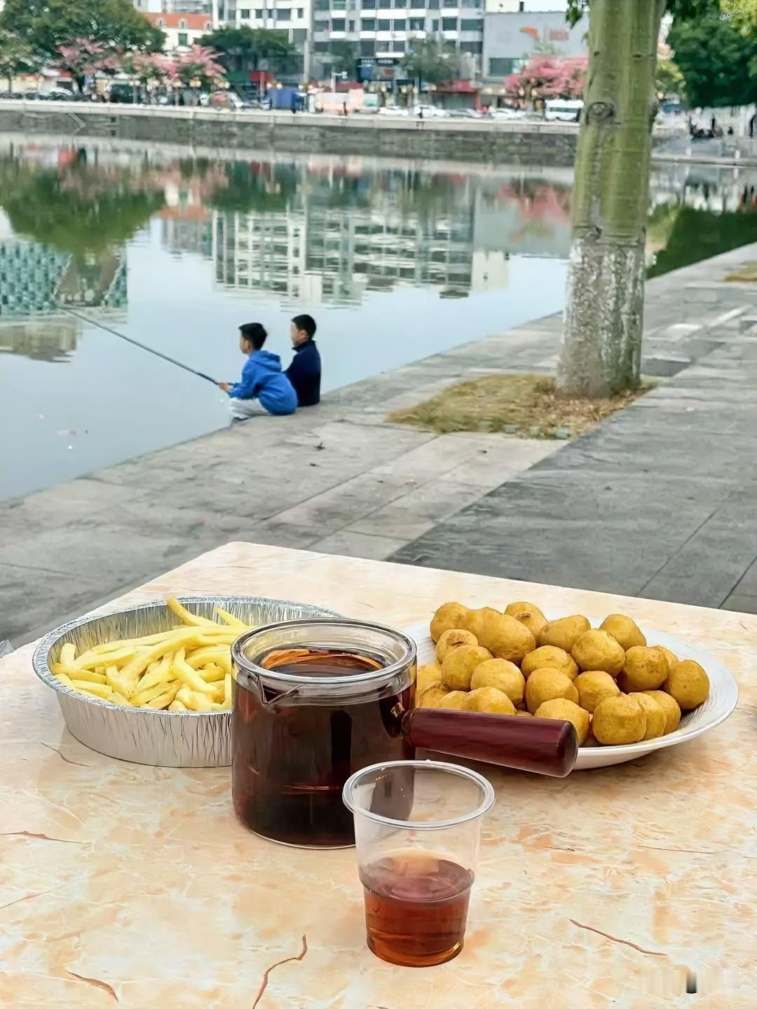 今天这局“湖边野餐”可太舒服了！刚把炸鱼丸、薯条摆上桌，抬眼就瞧见俩小孩蹲在
