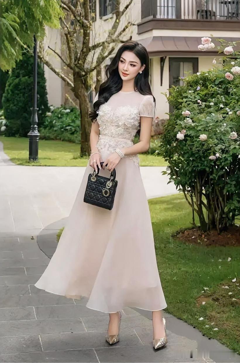 繁花簇拥间，浅杏纱裙曳地如流云。她执黑金手袋，眸光温婉含春，步履轻移，是庭院里悄