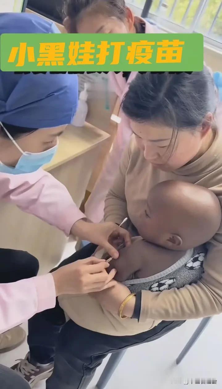 广东一名女子抱着一个小黑娃来医院里给孩子打疫苗。在注射的整个过程中，小黑娃不哭