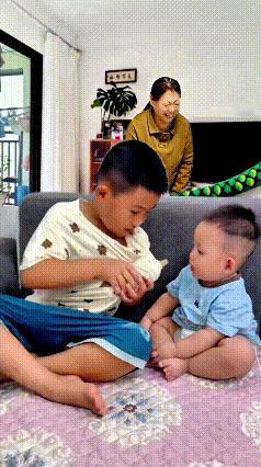 注意看！这小大哥真是闲不住，非要给弟弟喂奶喝。只见他把奶瓶藏自己衣服里，故意留个