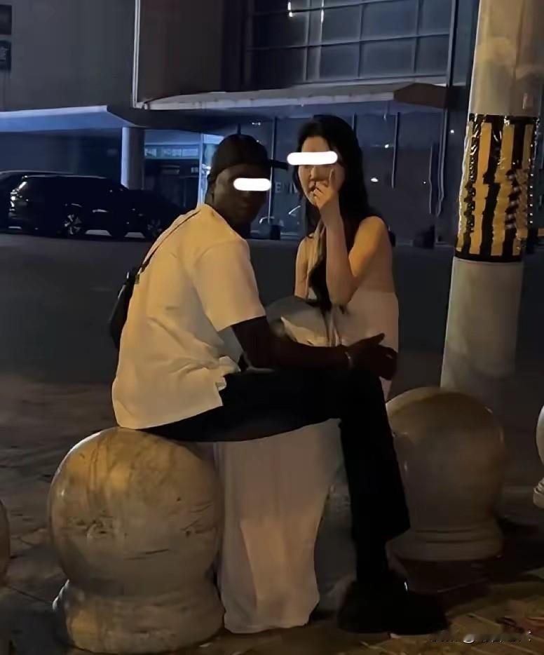 广州街头，半夜一位中国姑娘跟一个黑人男子坐在石墩上，黑人男子用手扶着姑娘的腰，正