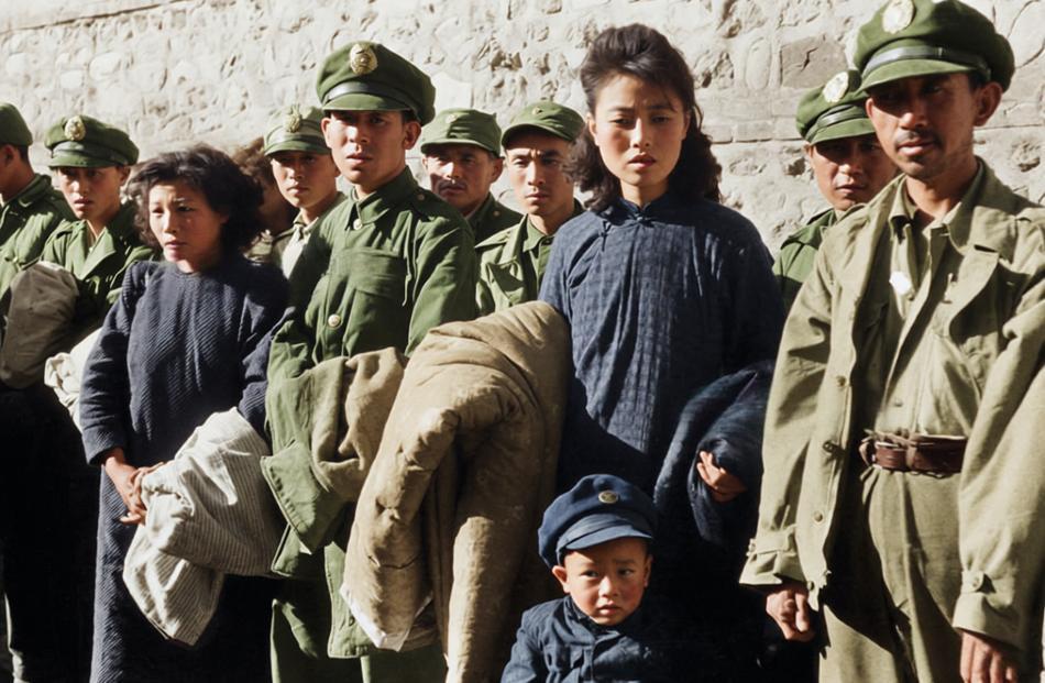 辽沈战役期间，一群国民党军官及其家属（包括妇女和儿童）排成一列，站在石墙前。军官