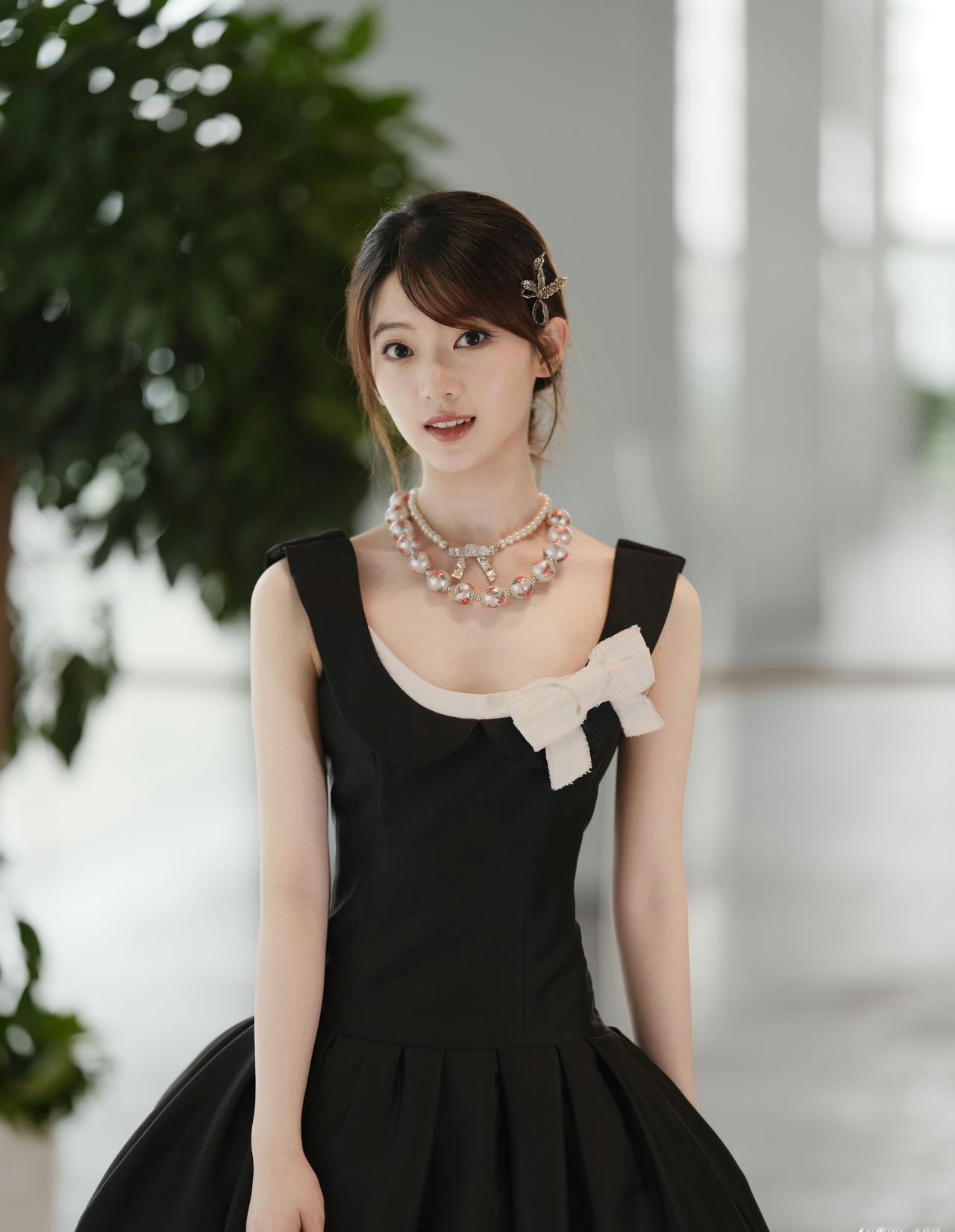 一袭黑裙勾勒优雅轮廓，胸前的白蝴蝶结点缀温柔，珍珠颈链衬出灵动气质。低挽的发