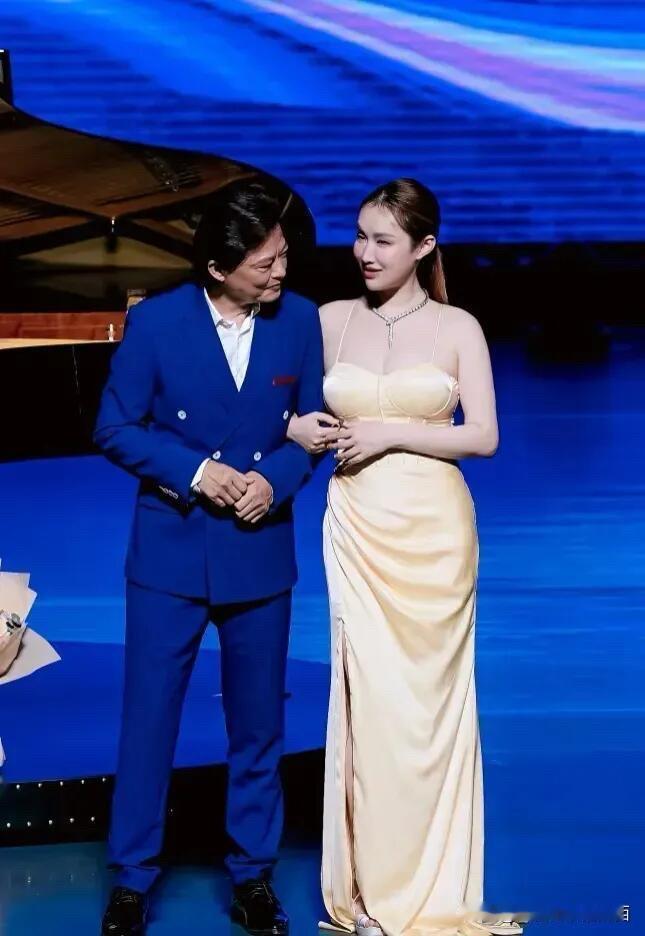 这是莫华伦和小娇妻在舞台上的一张合影，他的妻子比较年轻，风情万种，苗条身材，该凸