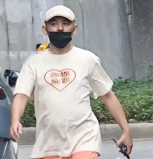黄子佼外出购物，他挺着大肚腩，戴着帽子和黑色口罩，拎着火锅店打包袋，表情严肃，肤