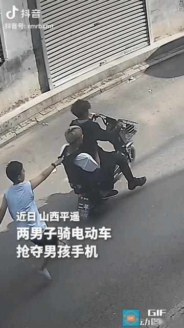 一名男孩在路边玩手机，这时，两名小伙骑电动车经过，抢走男孩的手机就迅速逃窜。男孩