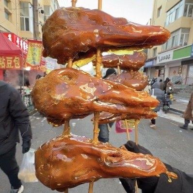 最近东北早市上出了个新鲜玩意儿——鸭头糖葫芦！一串30块，三个鸭头串一起，裹着亮