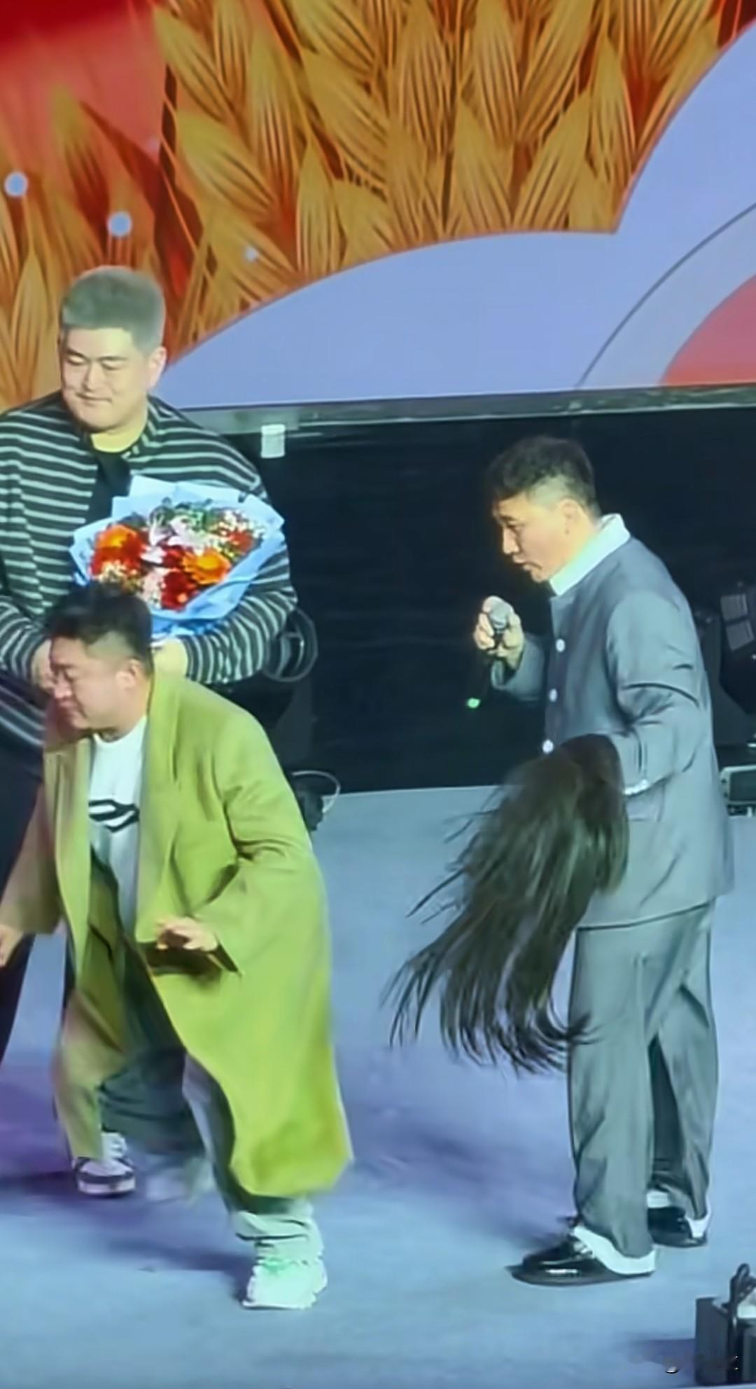 演出即将谢幕，一名长头发，身穿绿色大衣上台给大牛献花，完了搂着大牛脖子，腿夹着腰