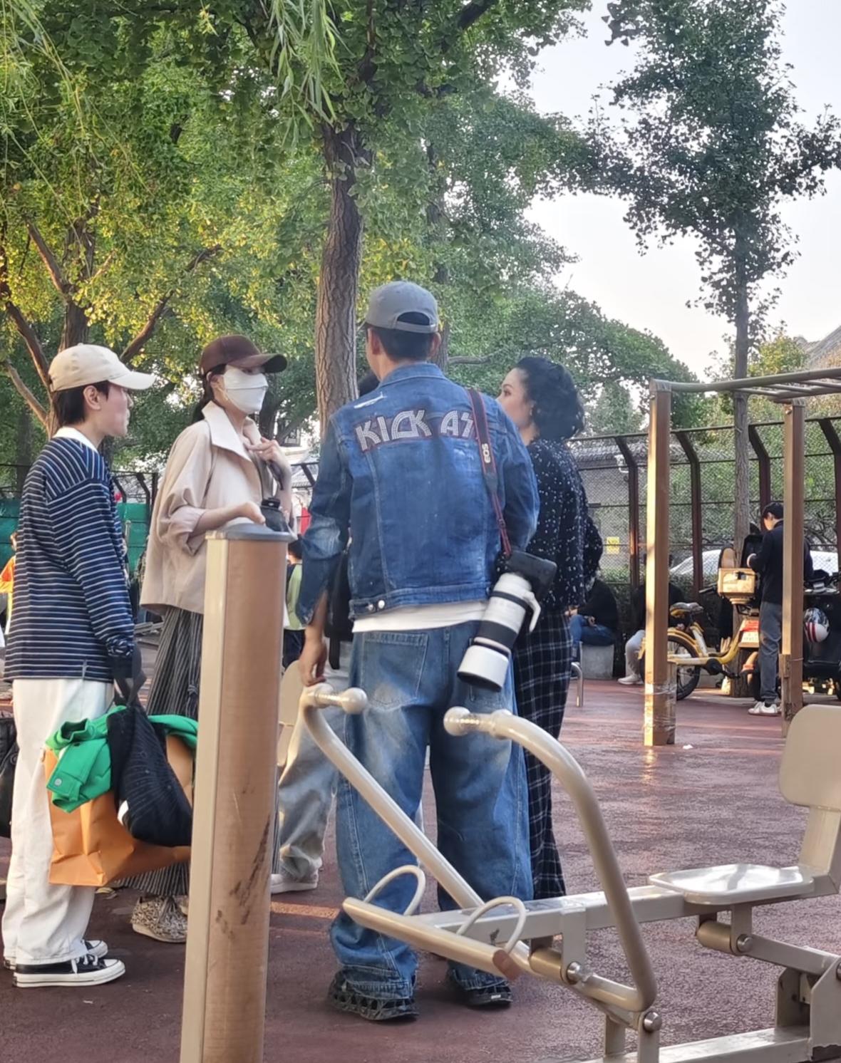 51岁郭晓东和老婆程莉莎在北京公园散步被偶遇，他背着一个长筒摄像机，在健身器械上