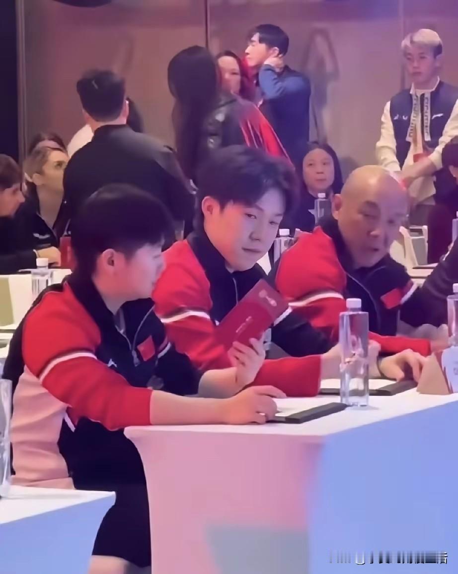 孙颖莎，王楚钦和光头肖战坐在一起抽签成都混团排位。远处的周到姐像明东厂的太监眼睛