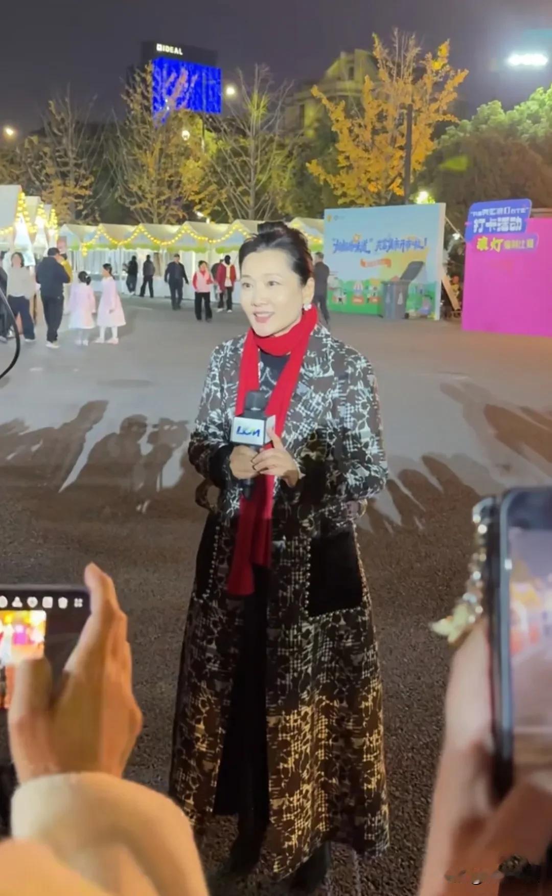 62岁的何赛飞老师，现身杭州出席活动，穿着一件拼色长大衣，带着红围巾，肤色白皙细