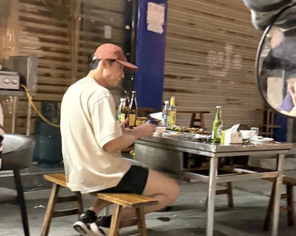 黄景瑜在乐山市一家路边摊吃烧烤，穿衣打扮很帅气，桌上放着好几瓶啤酒，路上人来人往