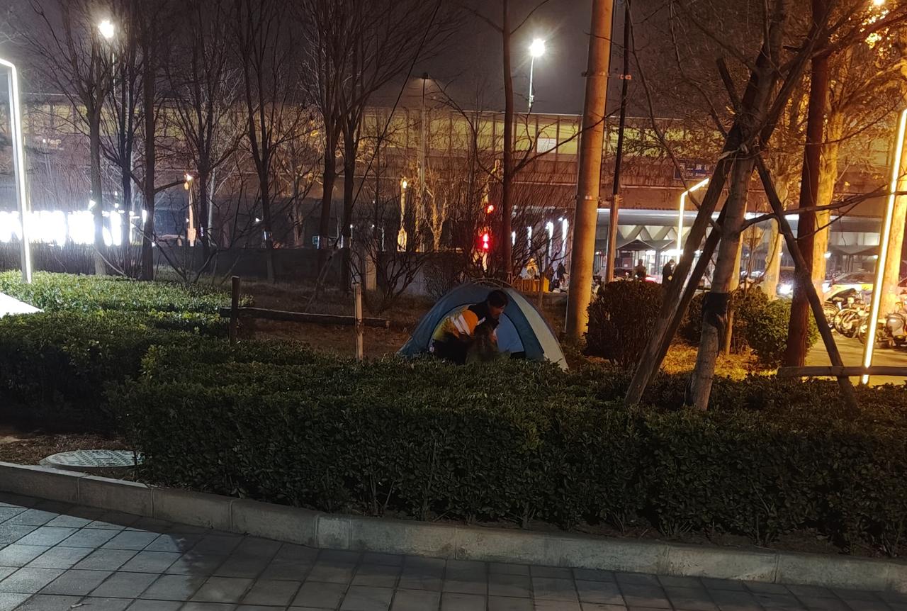 在北京海淀区西二旗地铁C口附近的安宁庄公园，大冬天里竟有外卖骑手在绿化带草坪上搭