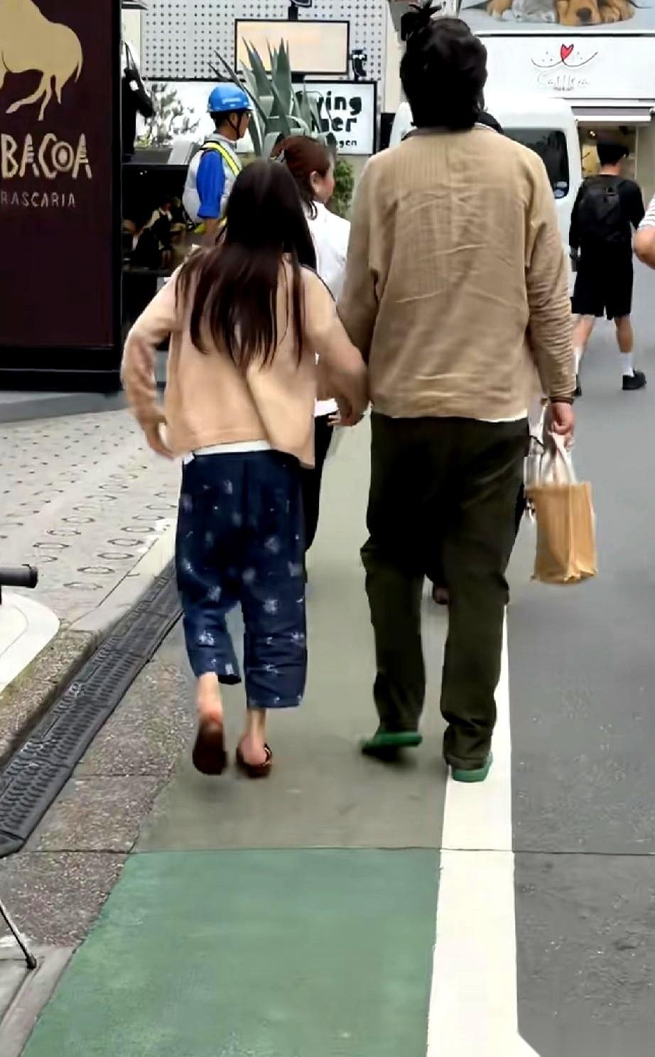 东京街头，一个男人牵着女儿的手走过。镜头拉近，他脚上是一双拖鞋，全身的衣服皱得