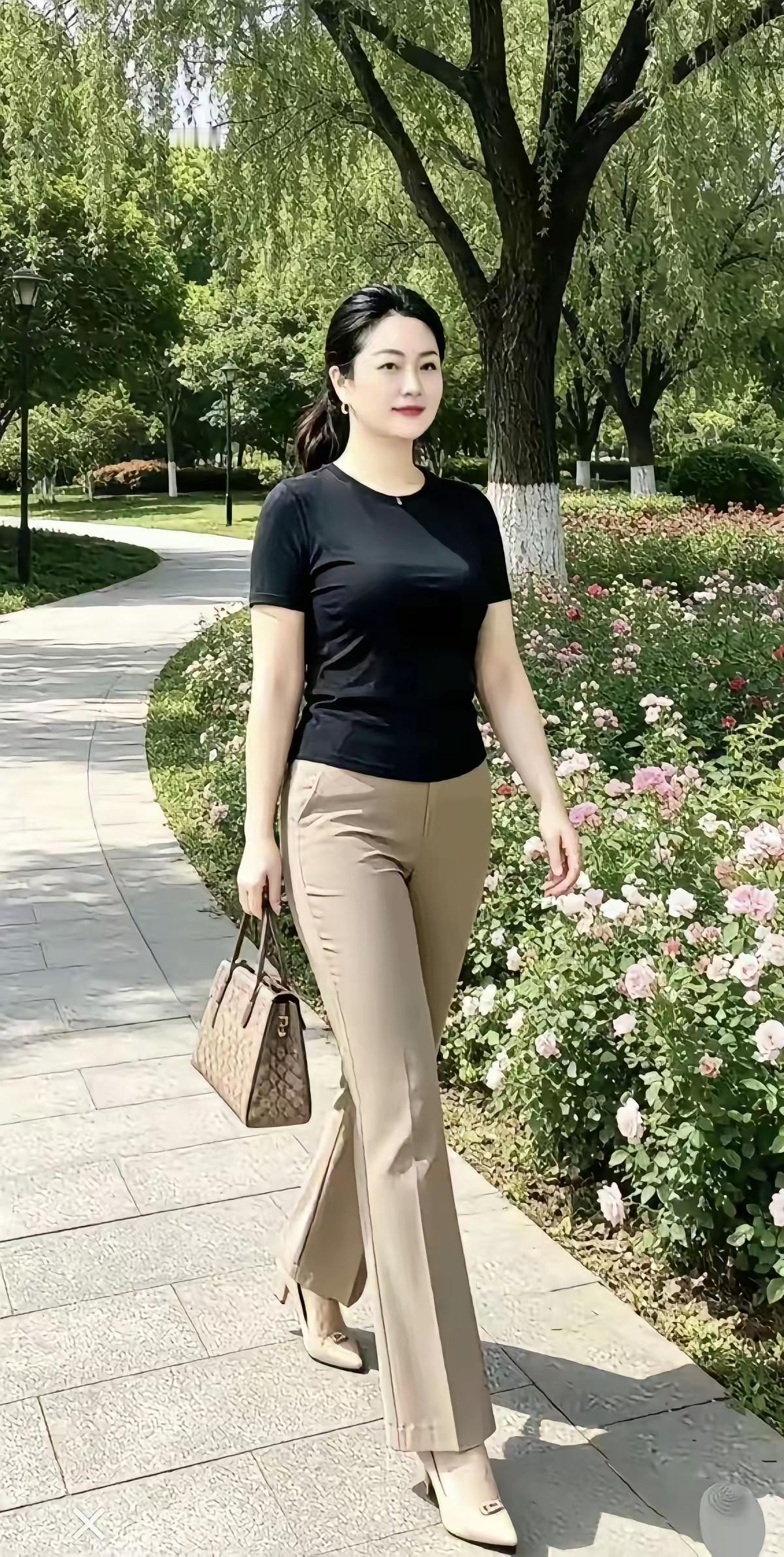 优雅漫步在花海中，黑色上衣与米色长裤的完美搭配，手提包点缀时尚气息。