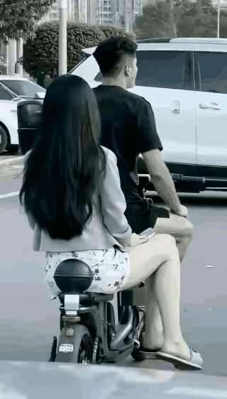 一位女子坐在老公的电动车上等红灯，听到后面汽车“嘀嘀”的鸣笛催促之声。女子回头一
